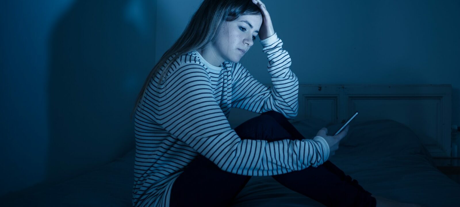 Sad teenager looking at her phone at night